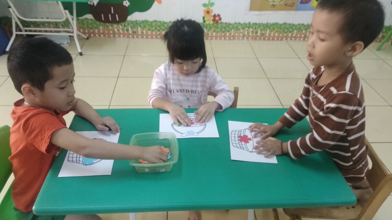 Các em học sinh được các cô hướng dẫn cách làm tranh dán hoa tặng mẹ.