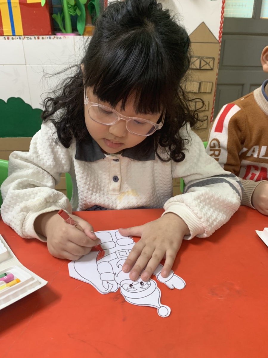 Học sinh lớp 5 tuổi A đang thực hiện tô màu hoàn thiện cho bức tranh ông già Noel của mình.